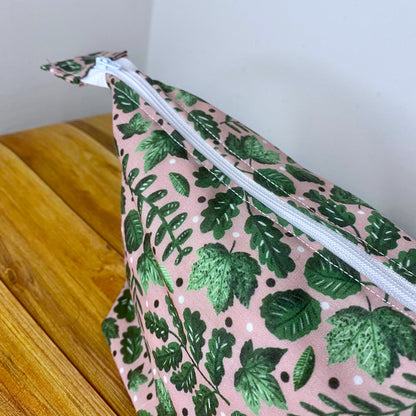Close up of the side of the makeup bag showing the vivid green of the leaves in the pattern. There is a wooden floor and white wall behind it,