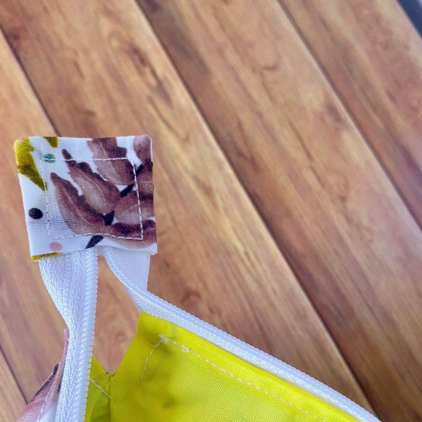 Closeup of the open zip of the makeup bag, showing the surface pattern design on the end of the zip, and the bright yellow lining on the inside.