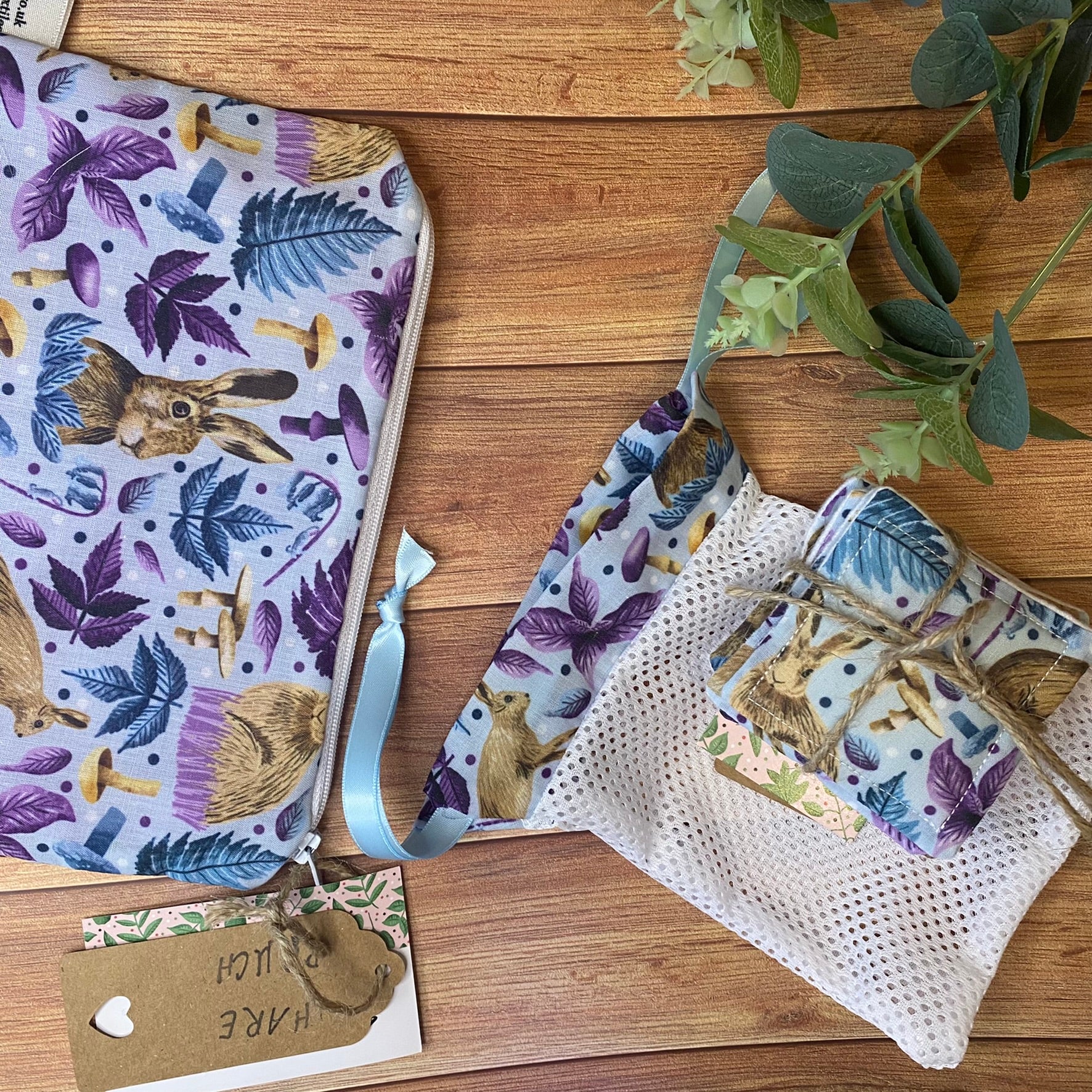 hare pattern in blue on a pouch, reusable skincare pads and a washbag, all sat on a wooden surface with foliage around it