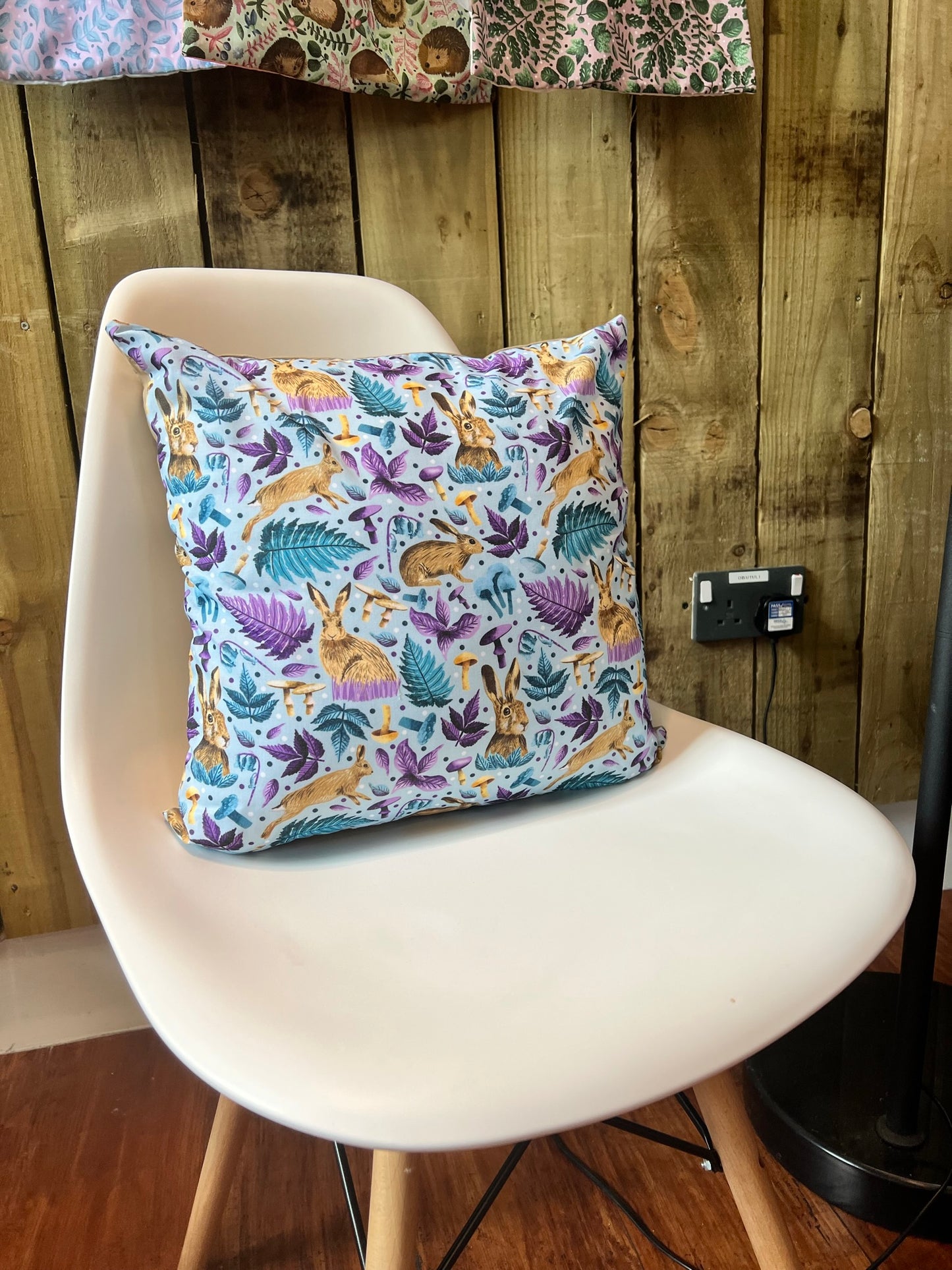 Our hare cushion cover is a fab rabbit gift for someone who loves the animals. It's shown here on a white chair with the bright blue pattern design. Ideal as a decorative pillow for a sofa