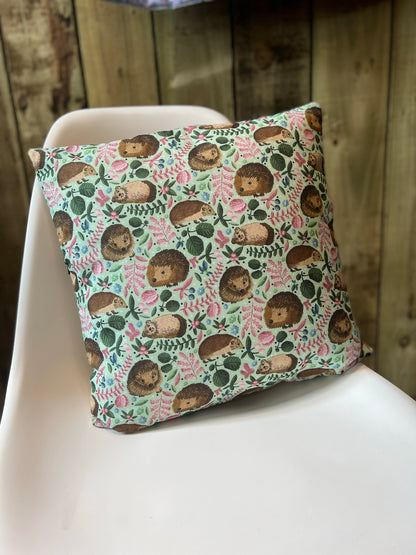 A great decorative cushion for bed, this hedgehog cushion makes a great hedgehog gift. It's shown here sat on a white chair with its hedgehog illustration on the front.