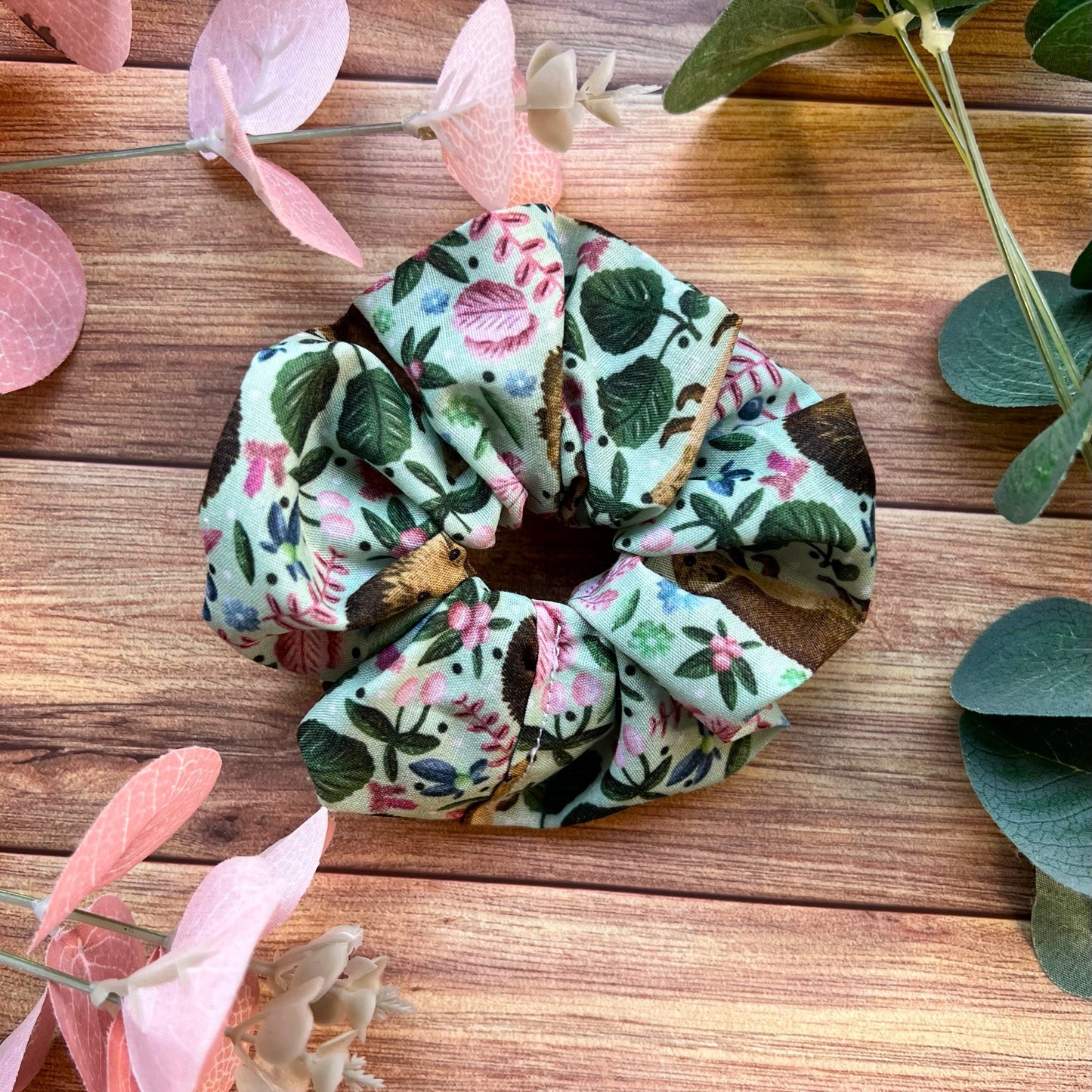  Closeup of hedgehog patterned scrunchie on a wooden backdrop with flowers and foliage around it