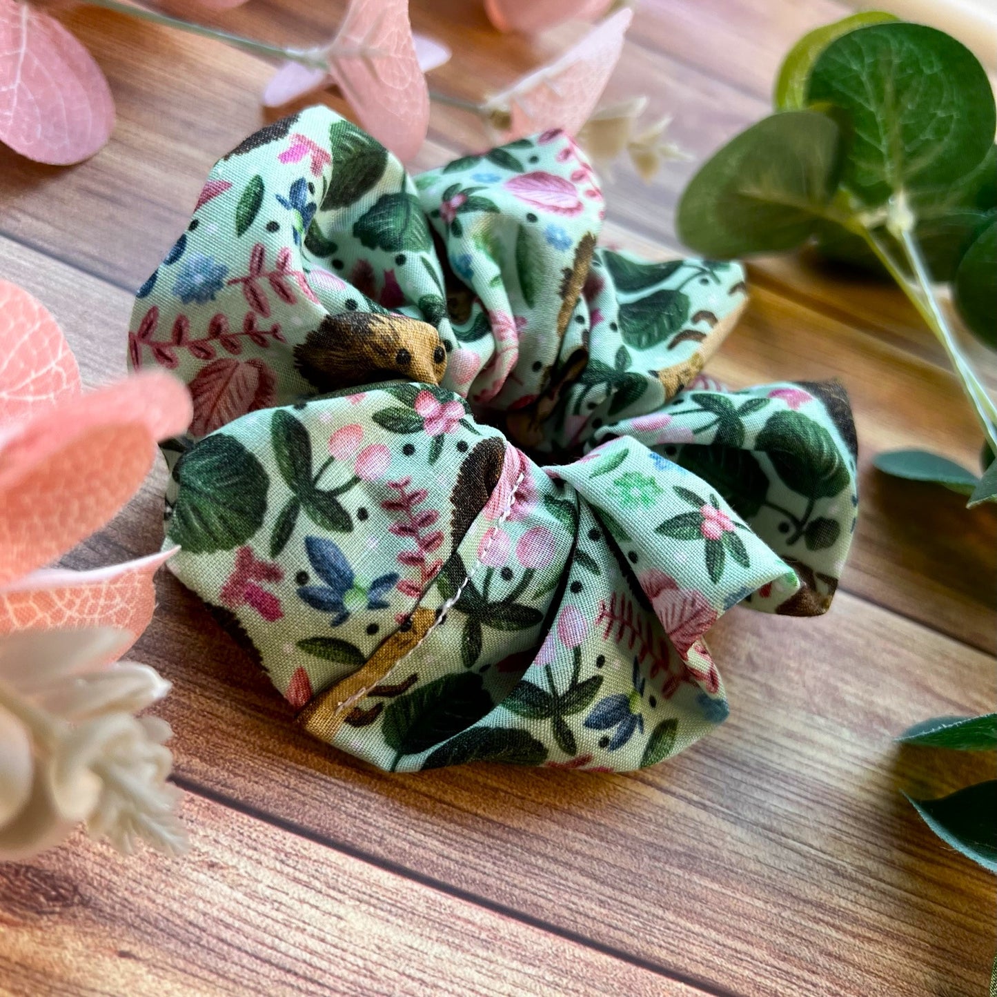 Closeup of hedgehog scrunchie amongst flowers and foliage on a wooden backdrop