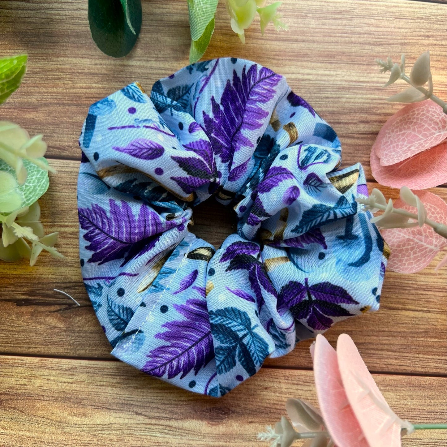 blue and purple hare patterned scrunchie sat on a wooden background with pink and green leaves around it