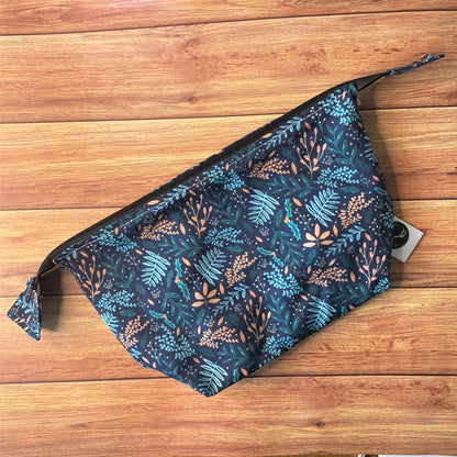 Dark foliage surface pattern design on a makeup bag, sat on a wooden background