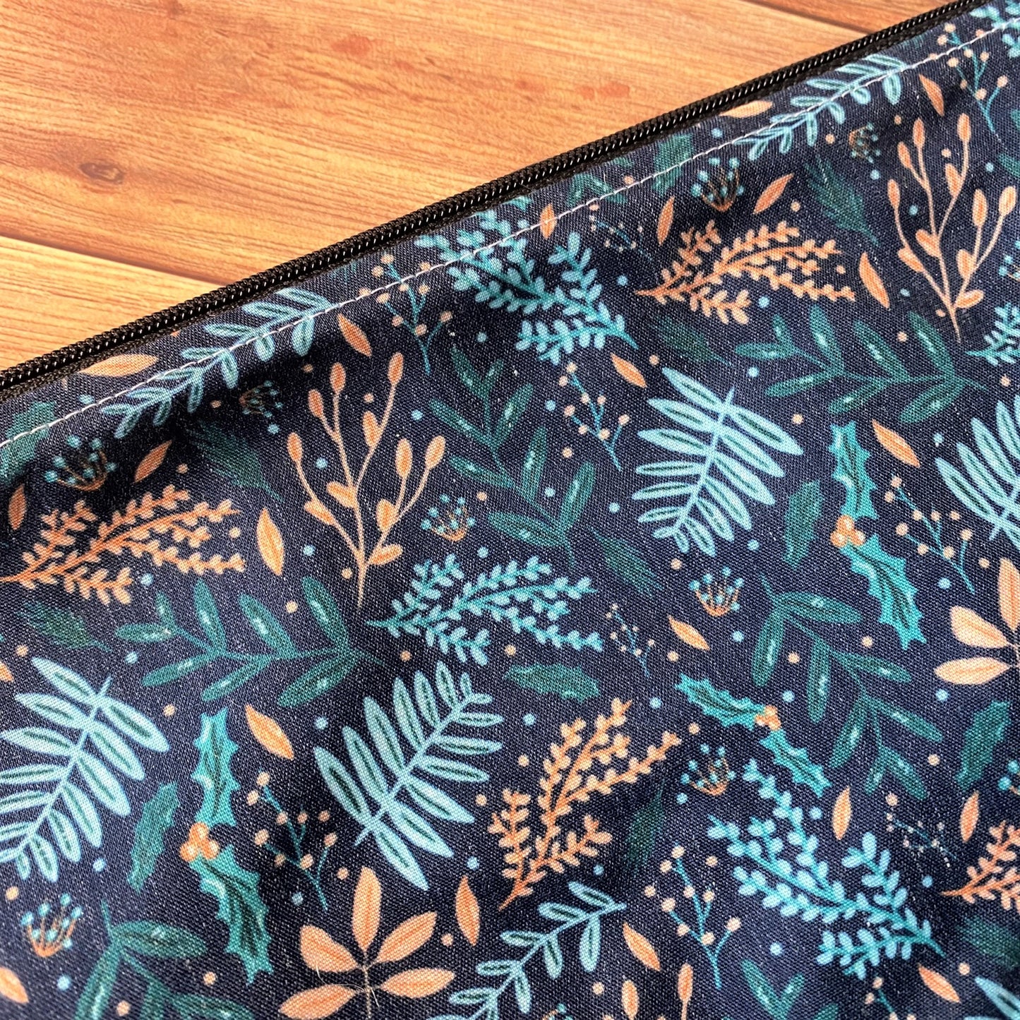 Closeup of the pattern design on the makeup bag. A mixture of light blue, peach and turquiose leaves on a dark blue background