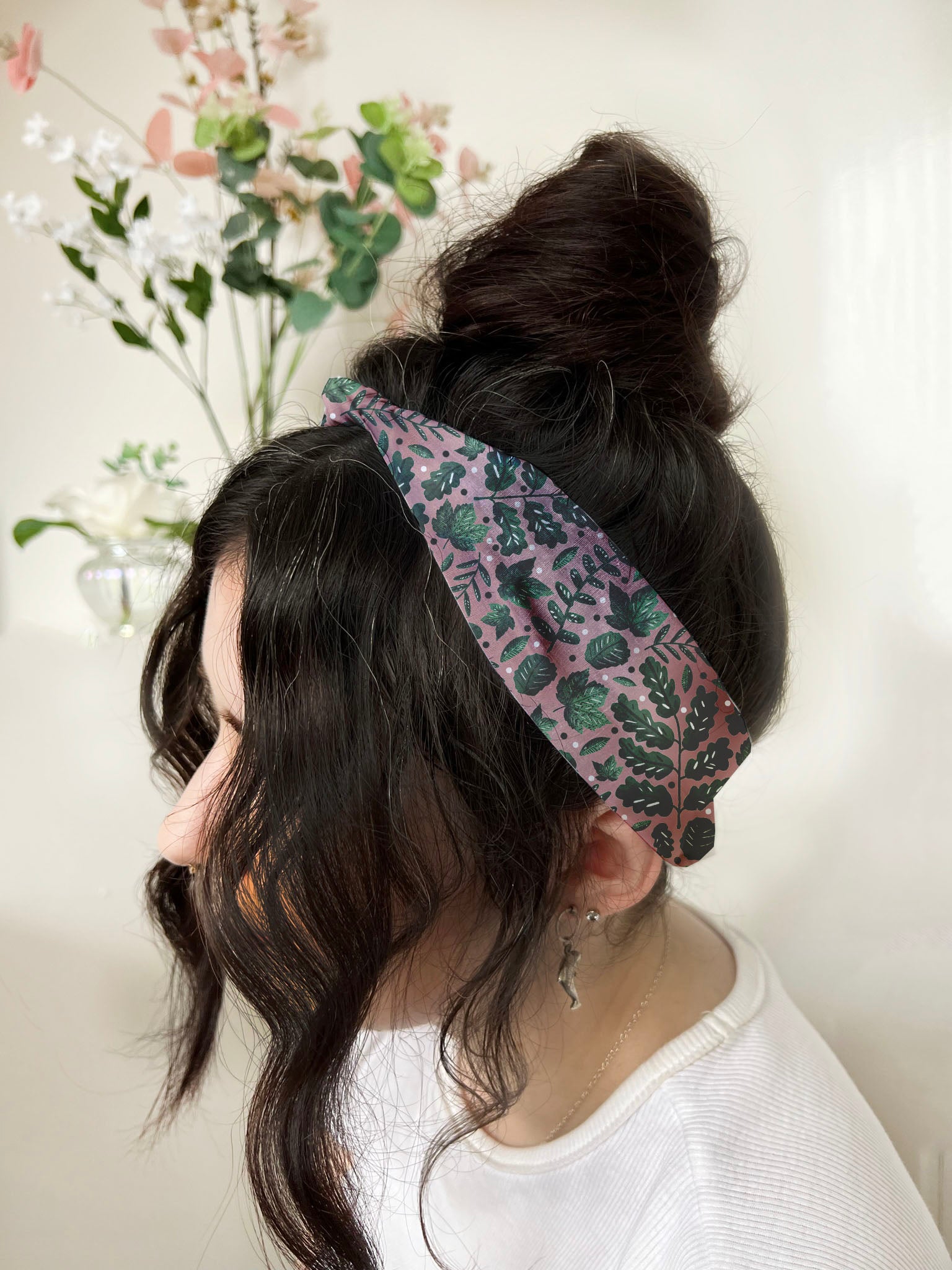 dark haired girl wears headband around her head with a bun in the back. The headband has a green foliage pattern illustrated on it. Shop gifts just because for her here.