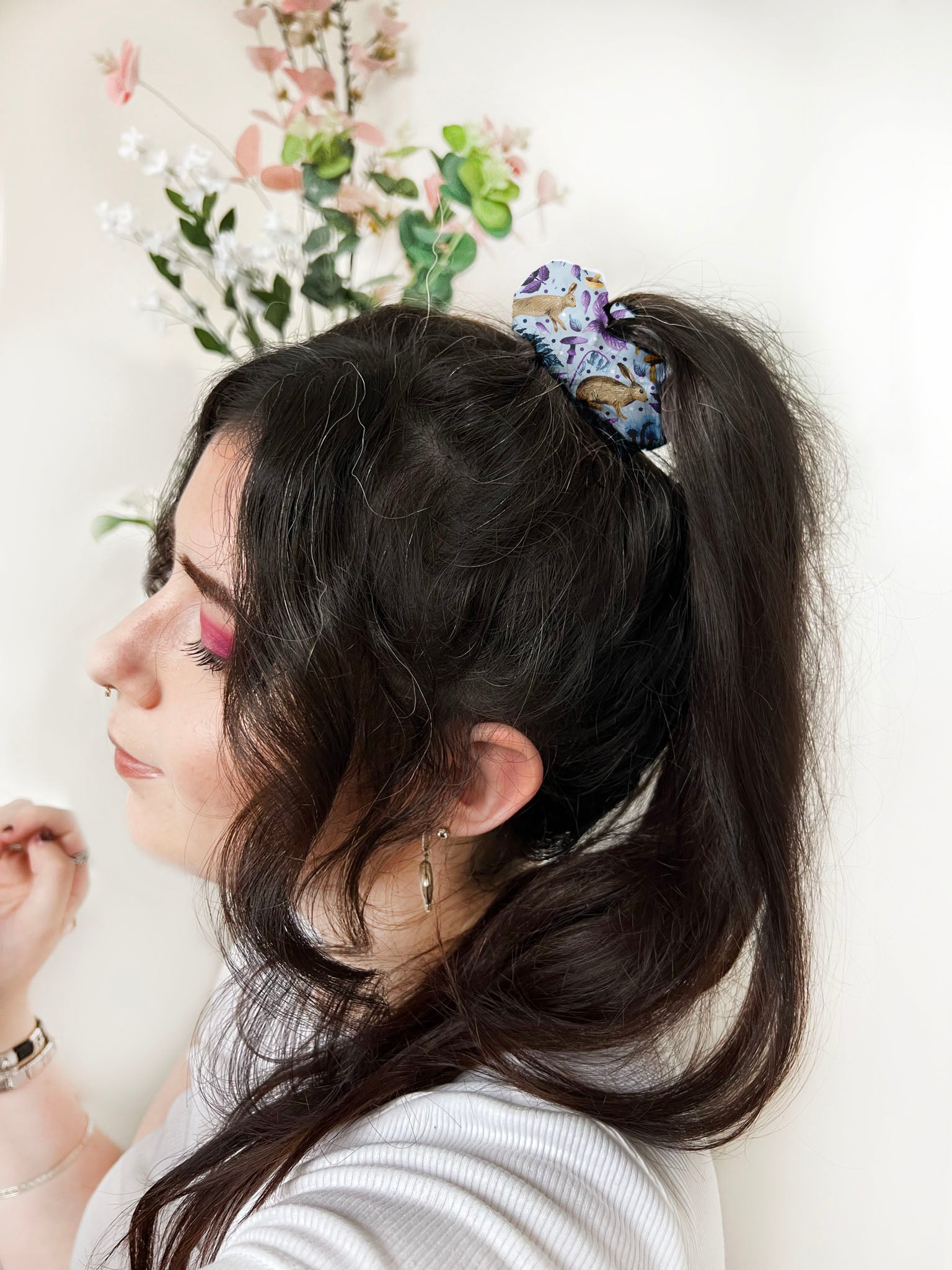 Dark haired girl faces the side with a hare patterned scrunchie holding a ponytail in on the back.