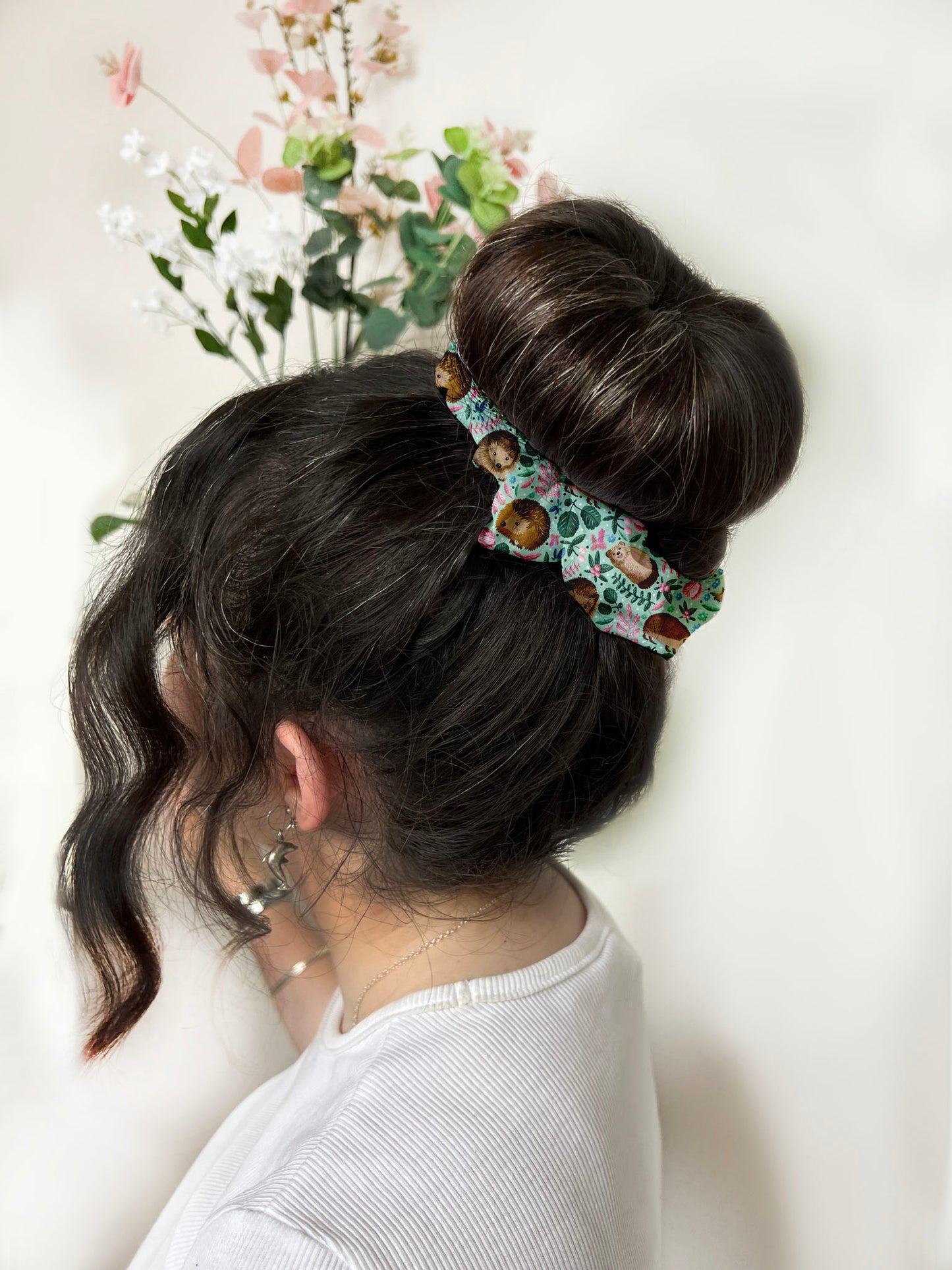 Dark haired girl wears scrunchie around a high bun. The scrunchie is green and has a hedgehog pattern on it.