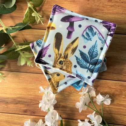 a stack of hare patterned reusable skincare pads photographed on a wooden background with foliage and flowers around them